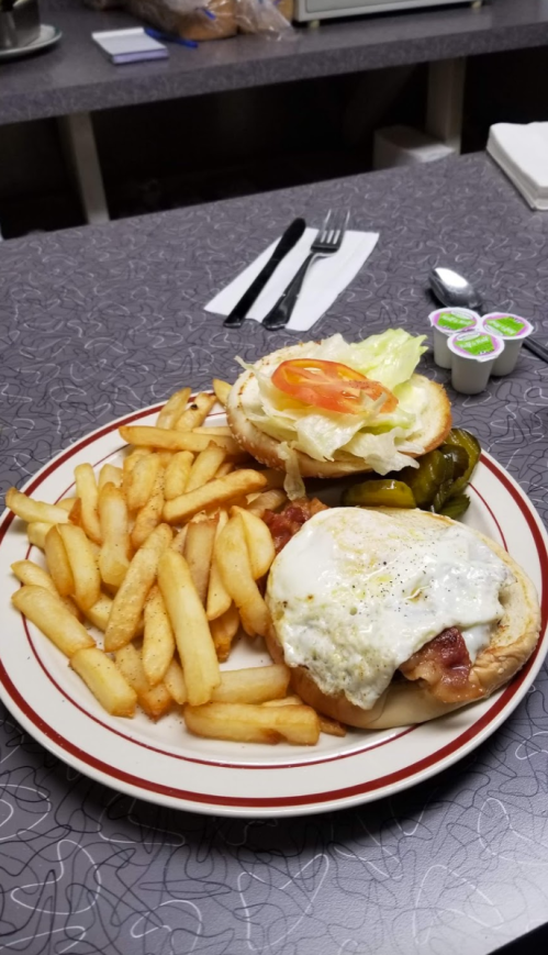 A plate with a burger topped with lettuce, tomato, and a fried egg, served with fries and pickles on the side.