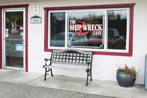 Exterior of the Ship Wreck Cafe, featuring a bench and a window with a red anchor logo.