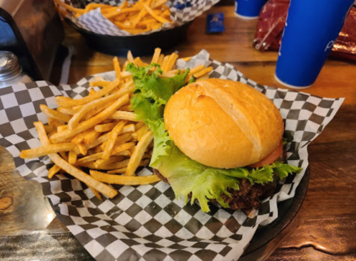 A burger with lettuce and tomato on a checkered plate, accompanied by a side of golden French fries.