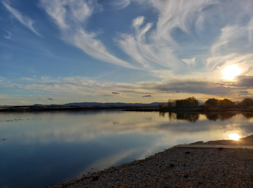 A serene lake at sunset, with colorful clouds reflecting on the water and mountains in the background.