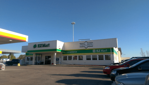 A convenience store named EZ Mart with a gas station, featuring clear skies and parked cars in the foreground.