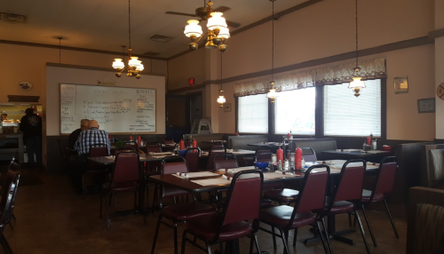 A cozy diner interior with red chairs, tables set for dining, and a chalkboard menu on the wall.