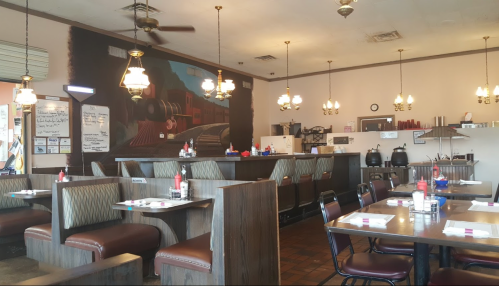 Cozy diner interior with wooden booths, a mural of a train, and vintage light fixtures. Tables set with condiments.