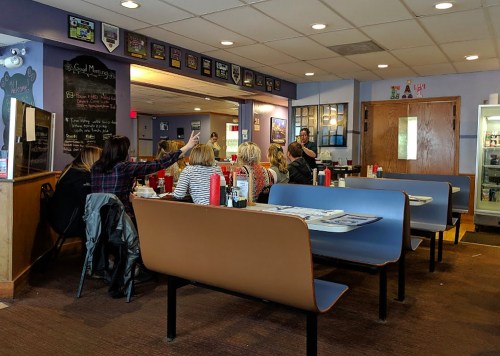 A cozy diner interior with booths, a group of people at a table, and a server interacting with customers.