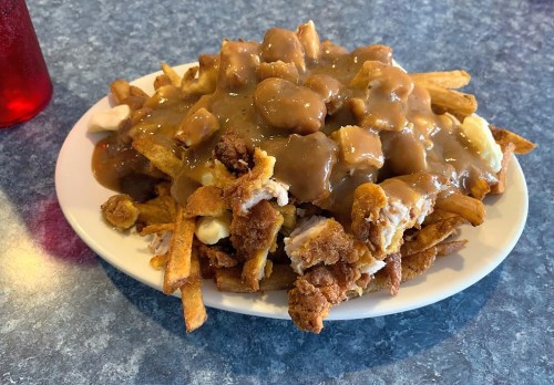 A plate of fries topped with chicken pieces and brown gravy, served on a blue table.