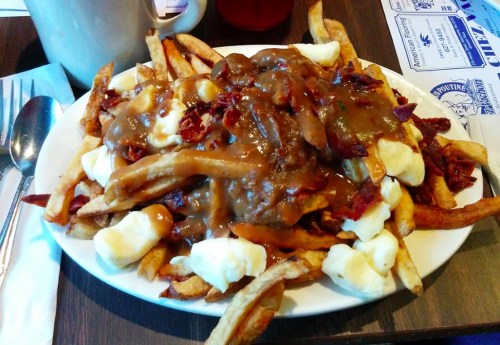 A plate of poutine topped with gravy, cheese curds, and crispy bacon over a bed of French fries.