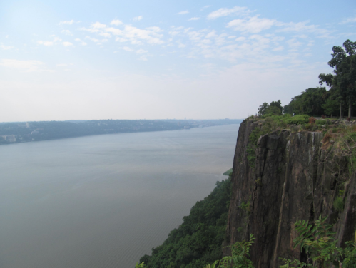 A scenic view of a river bordered by steep cliffs and lush greenery under a partly cloudy sky.