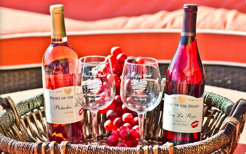 Two bottles of wine and two glasses sit in a woven basket, surrounded by grapes. The setting is warm and inviting.