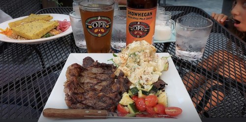 A plate of grilled steak with a side salad and potato salad, accompanied by a beer and a glass of water.