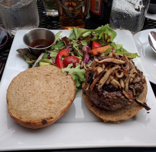 A plate with a burger on a whole grain bun, topped with mushrooms, alongside a fresh salad with mixed greens and tomatoes.