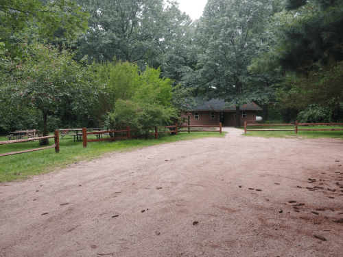 A gravel path leads to a cabin surrounded by trees and picnic areas in a serene outdoor setting.