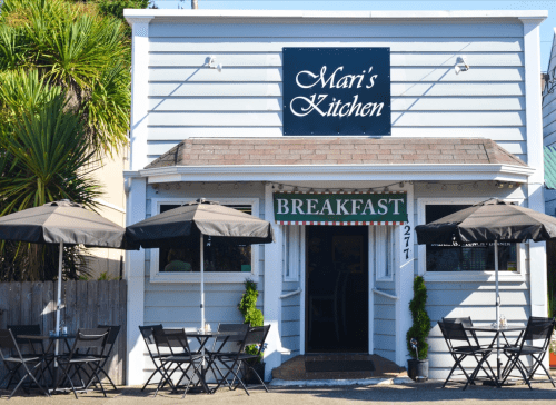 A cozy restaurant exterior with a sign reading "Mari's Kitchen" and outdoor seating under umbrellas.
