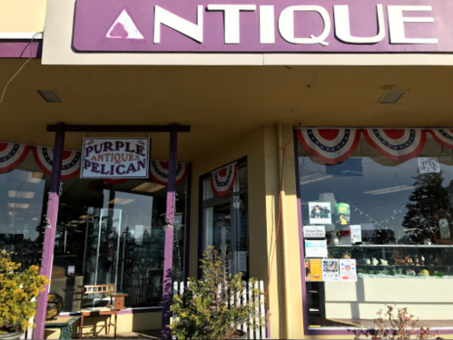 Exterior of a store named "Purple Antique Pelican," featuring a colorful sign and decorative bunting.