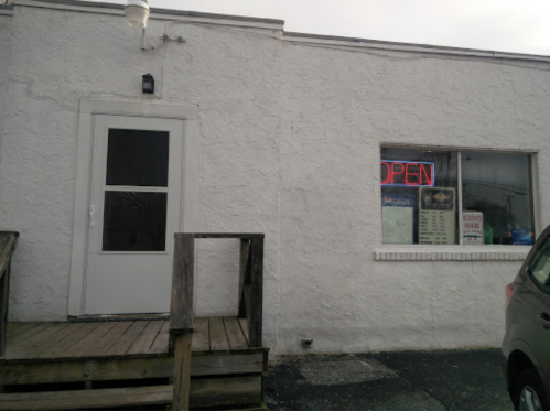 A white building with a wooden ramp, featuring an "OPEN" sign in the window.