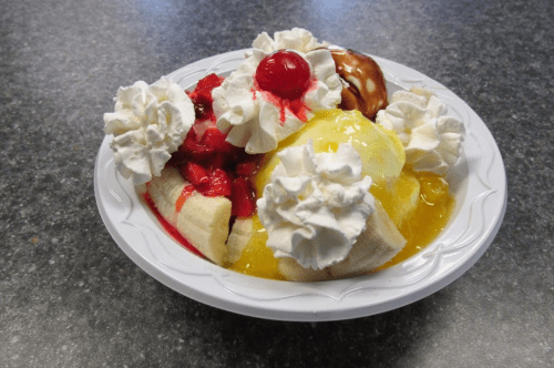 A dessert bowl with bananas, whipped cream, cherries, and colorful syrups.