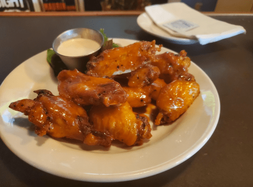 A plate of crispy chicken wings with a side of ranch dressing and a garnish of lettuce.