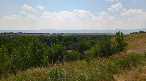 A scenic view of rolling hills and lush greenery under a partly cloudy sky. Mountains are visible in the distance.