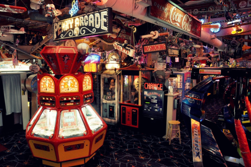 A vibrant retro arcade filled with vintage games, neon signs, and a penny arcade machine at the center.
