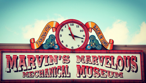 Sign for Marvin's Marvelous Mechanical Museum featuring a clock and colorful lettering against a blue sky.