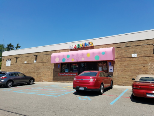 A storefront with a pink awning and colorful dots, labeled "Marvin's," surrounded by parked cars on a sunny day.