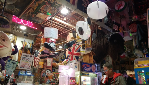 A colorful, eclectic shop interior filled with quirky decorations, signs, and a customer enjoying a drink.