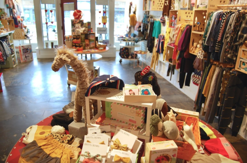 A colorful boutique filled with children's clothing, toys, and accessories displayed on tables and shelves.