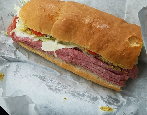 A large sub sandwich filled with layers of salami, lettuce, tomato, and cheese, resting on parchment paper.