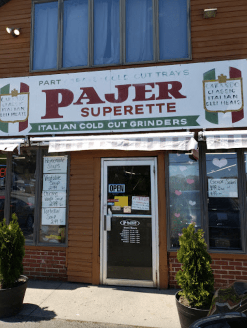 Exterior of Pajer Superette, featuring a sign for Italian cold cut grinders and an open door.
