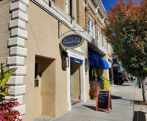 Exterior of a café with a sign reading "Collaborative Café," surrounded by colorful plants and a clear blue sky.