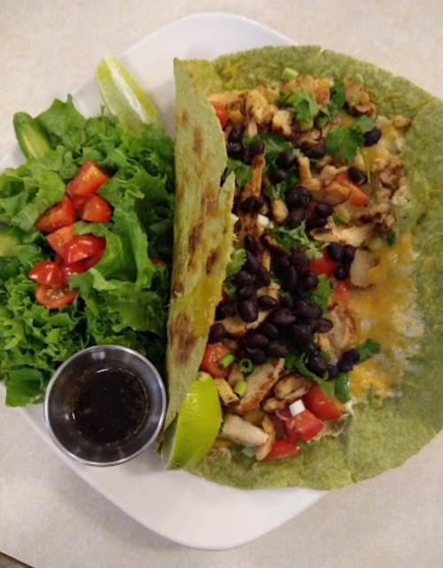 A large spinach tortilla filled with chicken, black beans, cheese, and veggies, served with a side salad and dressing.