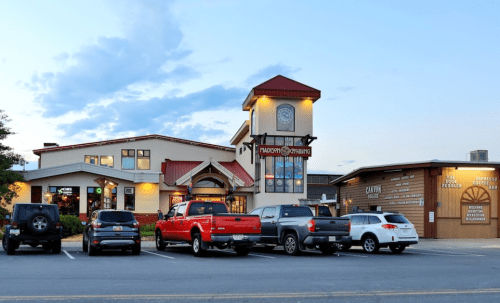 A restaurant with a clock tower, surrounded by parked cars, under a blue sky with scattered clouds.