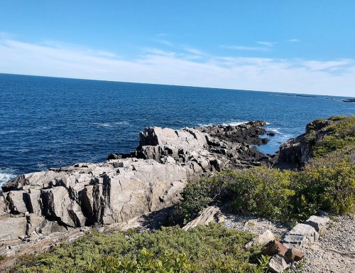 Rocky coastline with blue ocean and clear sky, featuring scattered greenery along the shore.