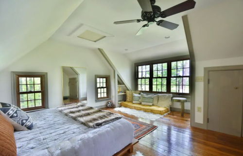 Cozy bedroom with a large bed, wooden floors, a sitting area by windows, and a rustic decor style.