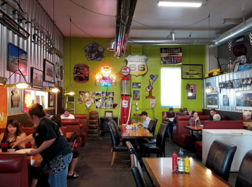 A vibrant diner interior with retro decor, booths, and patrons enjoying their meals. Neon signs and Route 66 memorabilia adorn the walls.