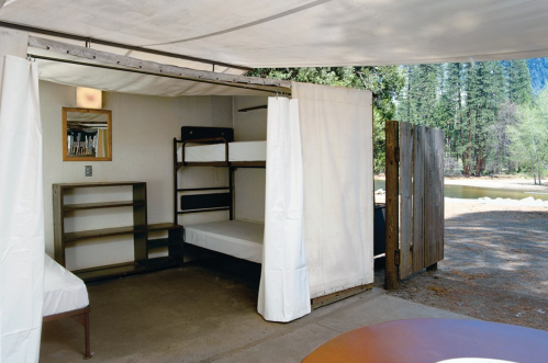 Interior of a simple cabin with bunk beds, a mirror, and a view of trees and a river outside.
