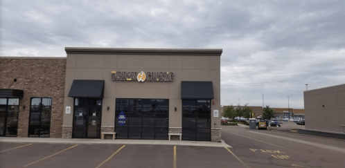 Exterior of Urban Buffalo restaurant with a gray facade and open sign, set in a shopping plaza under a cloudy sky.