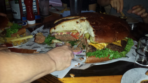 A giant burger with layers of lettuce, tomato, cheese, and a large patty, served with fries on a wooden table.