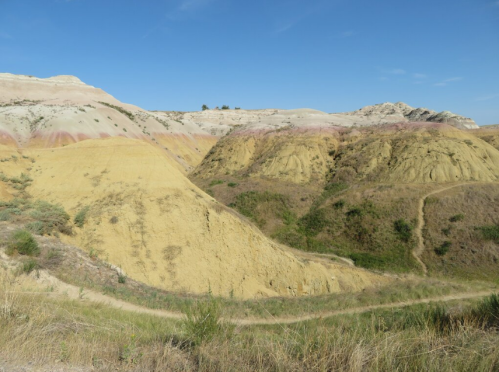 A scenic view of colorful, layered hills under a clear blue sky, with green vegetation along the slopes.
