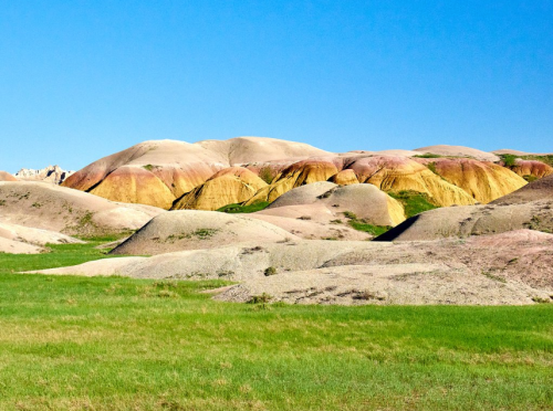 Colorful, rolling hills with shades of pink, yellow, and green under a clear blue sky.