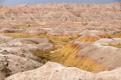 A vast landscape of colorful, layered hills and valleys in a rugged terrain under a cloudy sky.
