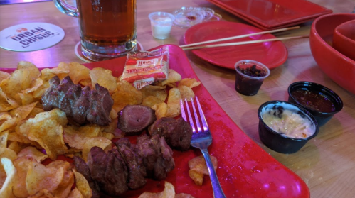 A red tray with chips, skewers of meat, dipping sauces, and a large beer in the background.