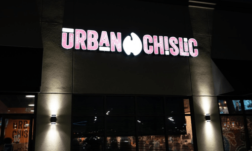Sign for "Urban Chislic" illuminated at night, with a modern storefront visible in the background.