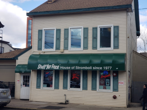 A two-story building with green shutters and an awning reading "Stuff Yer Face: House of Stromboli since 1977."