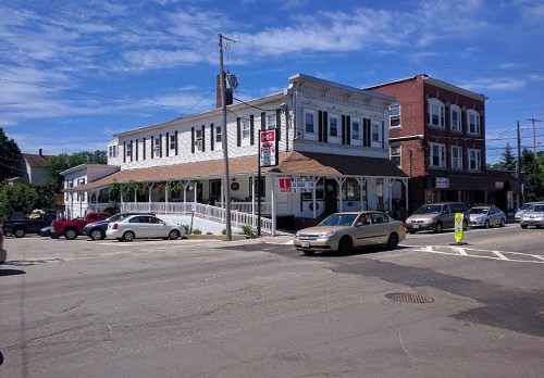 A street view of a two-story building with a restaurant and shops, surrounded by parked cars and a clear blue sky.