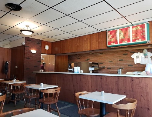 A cozy diner interior with wooden walls, a counter, menu board, and simple tables and chairs.