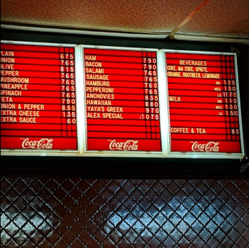 Menu board displaying various food items and prices, including pizzas, sandwiches, and beverages.