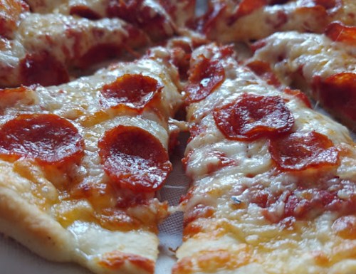 Close-up of a pepperoni pizza with melted cheese and crispy edges, showcasing several slices.