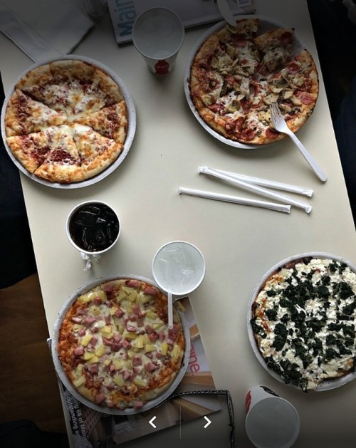 Four pizzas on a table, each with different toppings, alongside drinks and utensils.