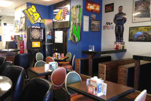 A cozy diner with racing-themed decor, featuring tables, chairs, and a dartboard on the wall.