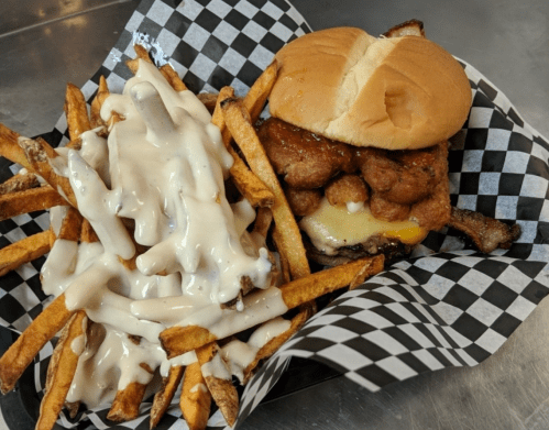 A sandwich with fried chicken and cheese, served with a side of loaded fries topped with creamy sauce in a checkered basket.